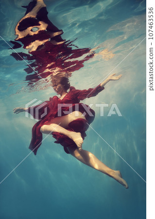 A woman in a red dress poses underwater as if she is flying 107463536