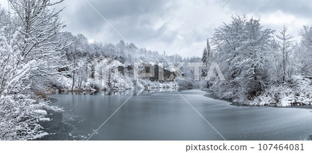Winter snowy landscape with a lake by rock wall. Winter snowy landscape with a lake by rock wall. 107464081