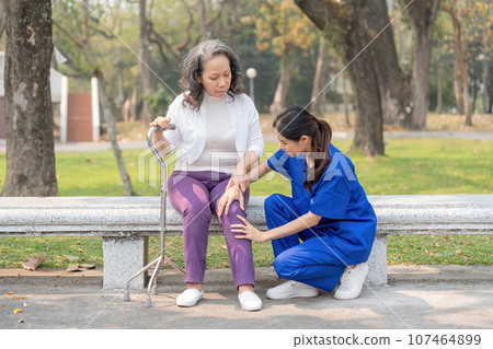 A female nurse or caregiver check the knee the elderly caring the hospital park A female nurse or caregiver check the knee the elderly caring the hospital park 107464899