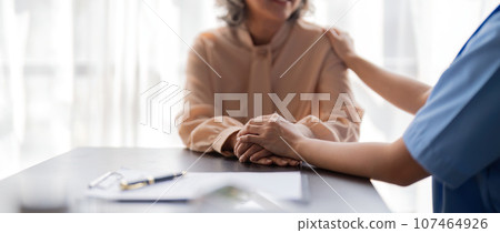 Female nurse hold her senior patient hand. Giving Support. Doctor help patient with disease. Female carer holding hands of senior woman Female nurse hold her senior patient hand. Giving Support. Doctor help patient with disease. Female carer holding hands of senior woman 107464926