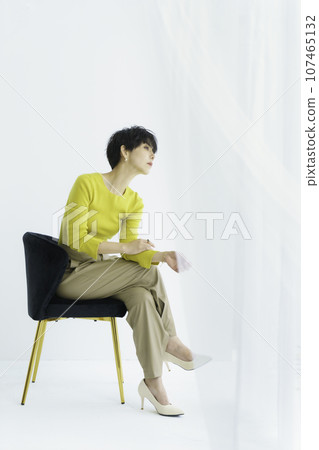 一位年輕女子坐在白色背景、垂直位置的椅子上的全身時尚肖像 107465132