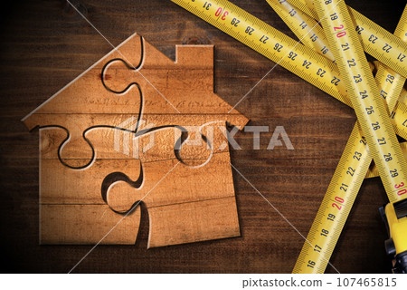 Tape Measures and a Wooden House made of Puzzle Pieces on Workbench Tape Measures and a Wooden House made of Puzzle Pieces on Workbench 107465815