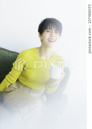 一位身穿黃色衣服的年輕女子坐在白色背景、垂直位置的綠色沙發上的時尚肖像 一位身穿黃色衣服的年輕女子坐在白色背景、垂直位置的綠色沙發上的時尚肖像 107466055