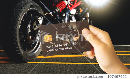 Hand holding a luxury credit or debit card with a motorbike on dark background Hand holding a luxury credit or debit card with a motorbike on dark background 107467621