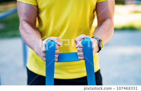 Man working out with resistance rubber bands in street, close up Man working out with resistance rubber bands in street, close up 107468331