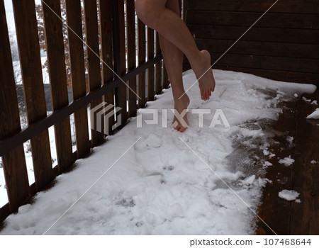 close-up shot. long bare feet stand on a snow-covered balcony close-up shot. long bare feet stand on a snow-covered balcony 107468644