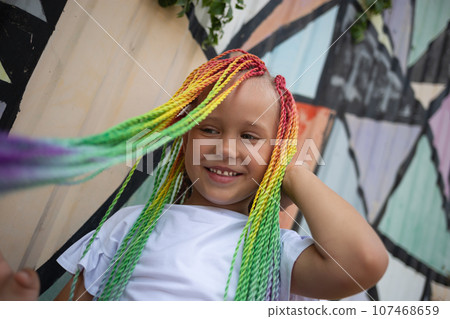 portrait of a little beautiful girl with multi-colored african braids on the background of a colorful wall 107468659