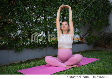 young beautiful pregnant woman practices yoga asanas on the green lawn outdoors. mindfulness and healthy lifestyle concept 107468689