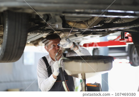 Auto mechanic checks running gear of car and oil leak at service station Auto mechanic checks running gear of car and oil leak at service station 107469380