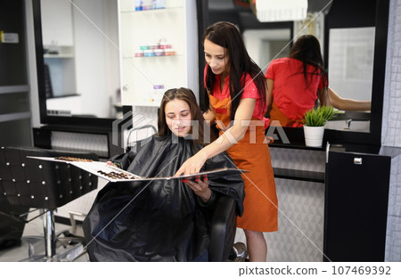 Professional female hairdresser and client choose hair dye color from hair color samples in hair salon 107469392