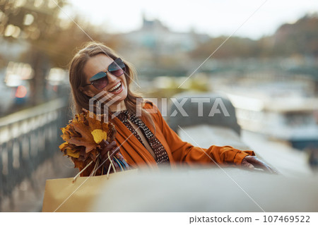 happy trendy woman in orange trench coat with shopping bags happy trendy woman in orange trench coat with shopping bags 107469522