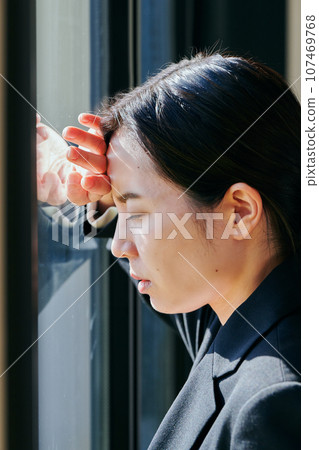 A young woman standing by the window and thinking with her eyes closed 107469768