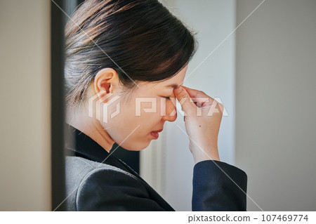 Young woman standing by the window and putting her hand between her eyebrows 107469774