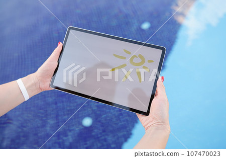 Female hands hold tablet with drawn sun and white screen above pool Female hands hold tablet with drawn sun and white screen above pool 107470023