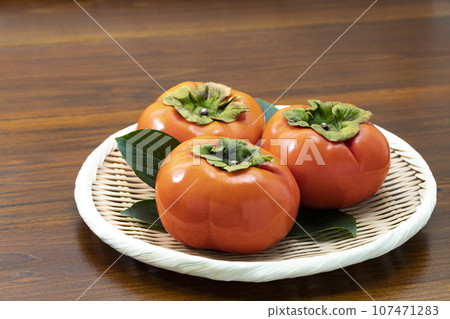 Autumn fruit persimmons placed on a tray and garnished with leaves Autumn fruit persimmons placed on a tray and garnished with leaves 107471283