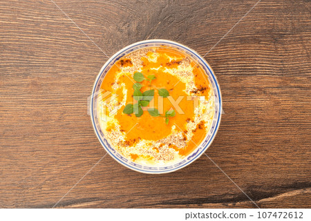 Top view of tomato puree soup with cream and basil leaves in a plate on a wooden background. 107472612