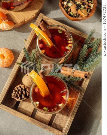 Spiced tea or mulled wine in glass cups with orange slices and cinnamon on a wooden tray. Top view, close-up. Spiced tea or mulled wine in glass cups with orange slices and cinnamon on a wooden tray. Top view, close-up. 107472725