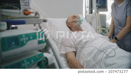 Friendly nurse adjusts life support machine for old patient Friendly nurse adjusts life support machine for old patient 107473277