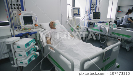 Sick elderly man in oxygen mask sleeps in bed in hospital ward Sick elderly man in oxygen mask sleeps in bed in hospital ward 107473310