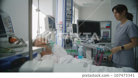 Friendly nurse adjusts life support machine for old patient 107473341