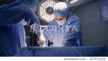 Medical staff at work in well-equipped operating room Medical staff at work in well-equipped operating room 107473420