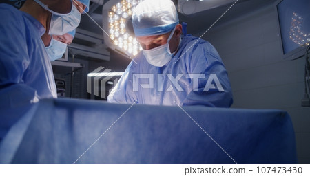 Medical staff at work in well-equipped operating room Medical staff at work in well-equipped operating room 107473430