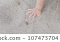 Baby enjoying putting his hands in sand at a beach. 107473704