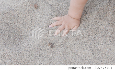 Baby enjoying putting his hands in sand at a beach. 107473704