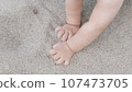 Baby enjoying putting his hands in sand at a beach. 107473705