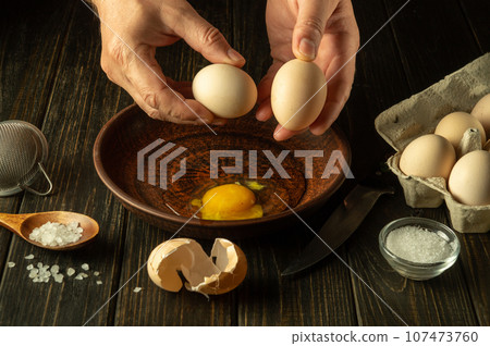 Egg breakfast by the hands of the chef in the kitchen of the restaurant. The process of cooking eggs on the kitchen table. Healthy eggs diet. Egg breakfast by the hands of the chef in the kitchen of the restaurant. The process of cooking eggs on the kitchen table. Healthy eggs diet. 107473760