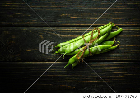 Beans in pods tied with a thread in a bunch on a wooden black table. Fresh beans after harvest are prepared for sale 107473769