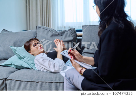 Female psychologist having therapy with middle-aged woman patient in office 107474335