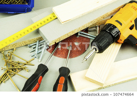 tools for repair and construction. Screwdriver, furniture screws, measuring tape, self-tapping screws, with a place for text. Top view tools for repair and construction. Screwdriver, furniture screws, measuring tape, self-tapping screws, with a place for text. Top view 107474664