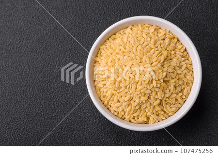 Raw whole grain orzo pasta as an ingredient for a delicious dish 107475256