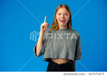 Young teenager girl pointing up with finger on blue background 107475671