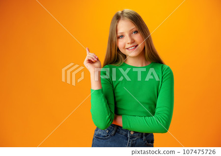 Teenager girl over yellow background pointing finger to copy space Teenager girl over yellow background pointing finger to copy space 107475726