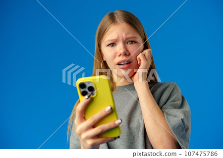 Worried teen girl checking bad news on smartphone in studio Worried teen girl checking bad news on smartphone in studio 107475786