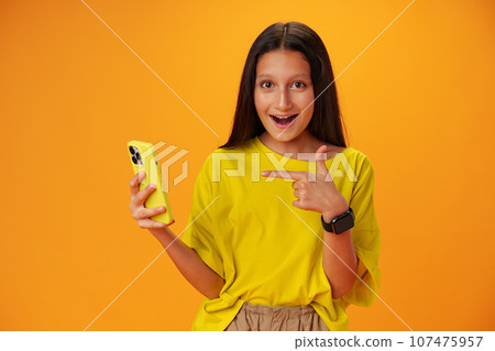 Stylish teen girl using smartphone over yellow background in studio 107475957