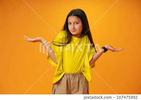 Puzzled teen girl don't know what to do on yellow background in studio Puzzled teen girl don't know what to do on yellow background in studio 107475992