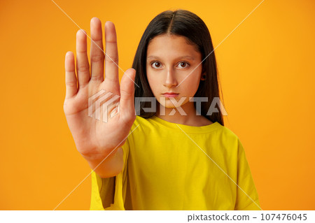Teen girl extend hand in block gesture against yellow background Teen girl extend hand in block gesture against yellow background 107476045
