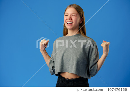 Portrait of a joyful happy teenage girl celebrating success on blue background Portrait of a joyful happy teenage girl celebrating success on blue background 107476166