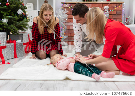 Parents play with their baby girl lying on the carpet 107476668