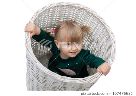 A little girl plays while sitting in a large wicker basket. A little girl plays while sitting in a large wicker basket. 107476685