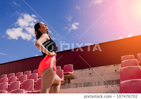 A female coach with dark hair stands on the red running track of the stadium A female coach with dark hair stands on the red running track of the stadium 107476702