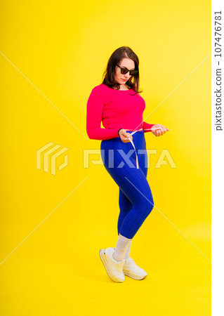Overweight woman measuring waist before weight loss in studio shot on yellow background 107476781