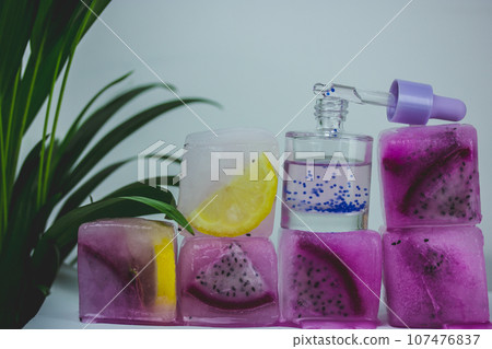 Cosmetic serum glass bottle with pipette on ice cubes with fresh pitaya, citrus 107476837