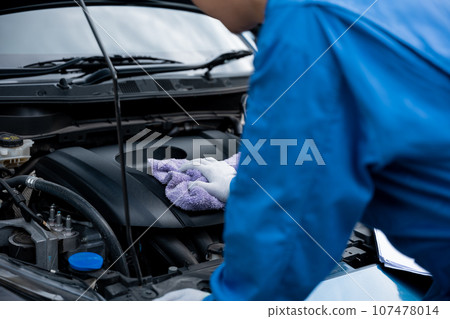 Close-up shot of an Asian mechanic's hand in a blue shirt writing on a paper, in an auto repair shop. 107478014