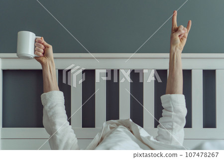 Wonderful start to new day. Unrecognizable man wakes up and stretches , holding cup of fragrant coffee in his hands. 107478267