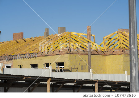 Construction of the roof of the house against the background of the blue sky. Construction of the roof of the house against the background of the blue sky. 107478610