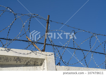 Barbed wire on top of a concrete fence. 107478611